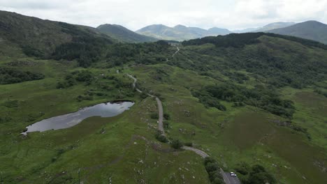 aerial shot of the lush ladies view in ireland with a winding road and a pond, under overcast skies