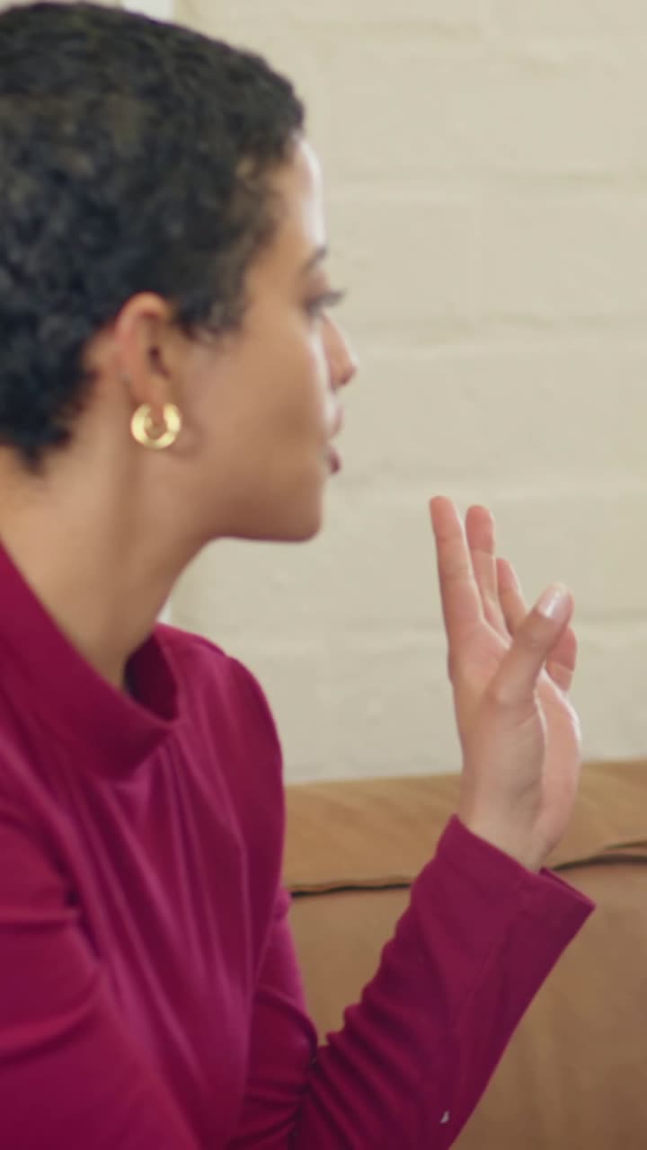 Vertical video: Replying offframe prompt woman gesturing saying on tan sofa, maroon top, copy space