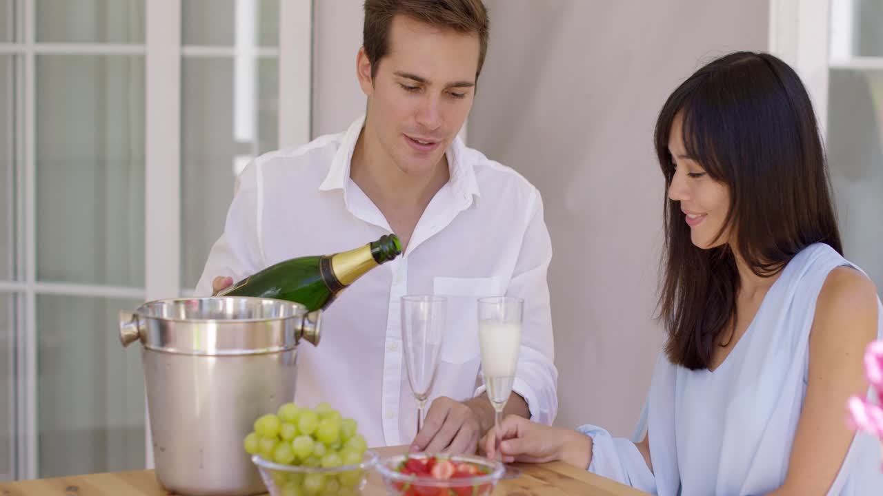 pareja joven sonriente sirviendo champán para beber