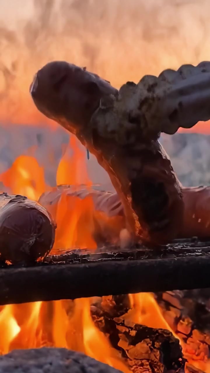 Des saucisses grésillantes sur une flamme nue sur fond de coucher de soleil magnifique, capturant l'essence de la cuisine en plein air et la chaleur du feu.