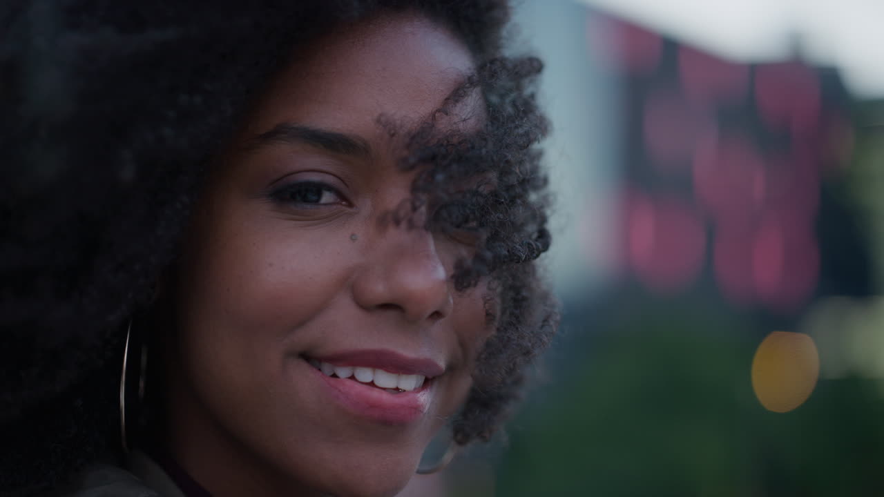 retrato de cerca hermosa joven mujer afroamericana sonriendo segura independiente mujer negra disfrutando de un estilo de vida relajado en la ciudad el viento soplando peinado afro