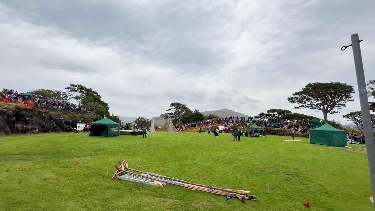 Wide shot of grassy field with cabers, spectators, and overcast sky at Scottish festival