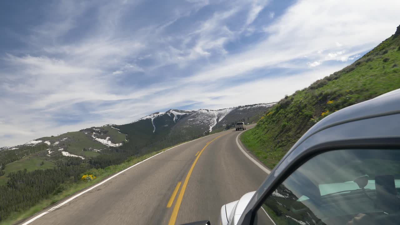 Cámara fuera de una camioneta blanca viajando por una carretera de montaña en verano