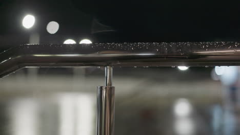 vorwärtsblick auf einen regenbedeckten metall-handrail in der nacht, mit wassertropfen, die unter sanfter beleuchtung glänzen