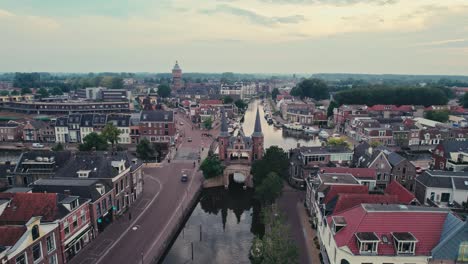 A-quaint-european-town-with-a-canal-during-early-evening,-red-roofed-houses,-distant-church,-aerial-view