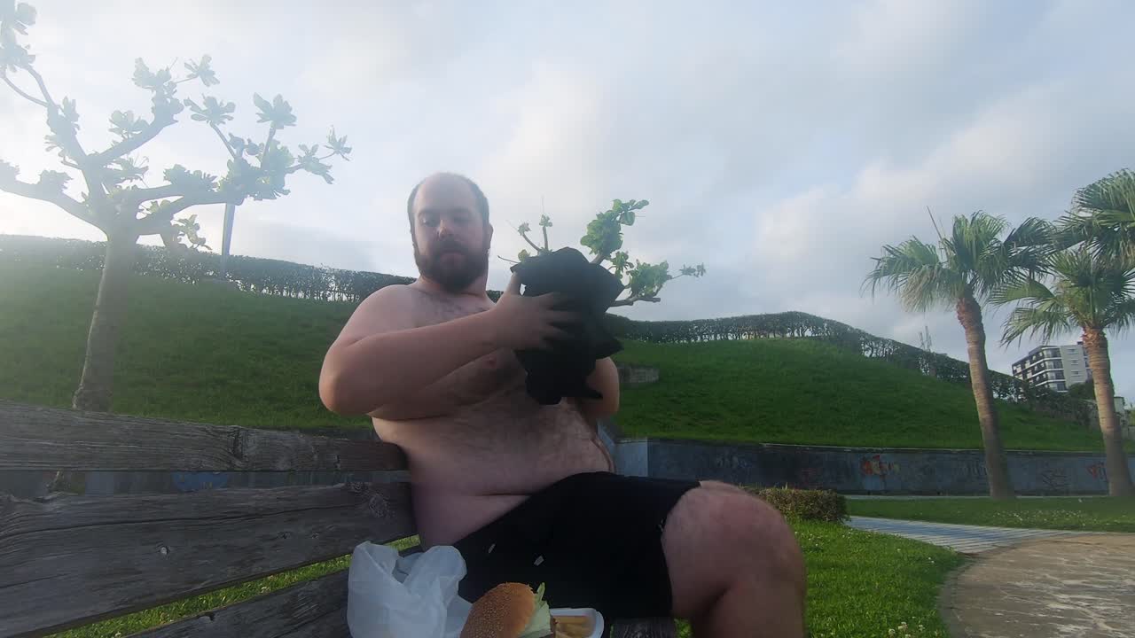 후퇴 헤어 라인을 가진 추악한 비만 남자는 뚱뚱한 털이 배를 드러내는 그의 검은 셔츠를 제거합니다