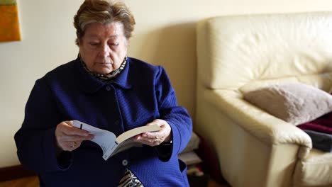 old woman reading book at home in living room, then puts it down