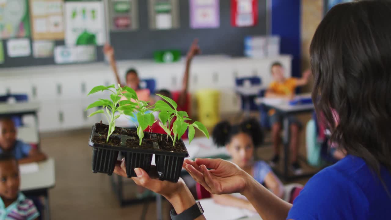 maestra de raza mixta de pie en el aula haciendo preguntas sobre plantas durante la lección de biología