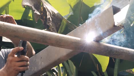 professional welder employing industrial welding machine to put together two pieces of metal creating a metalic structure as part of his daily work at a local small business