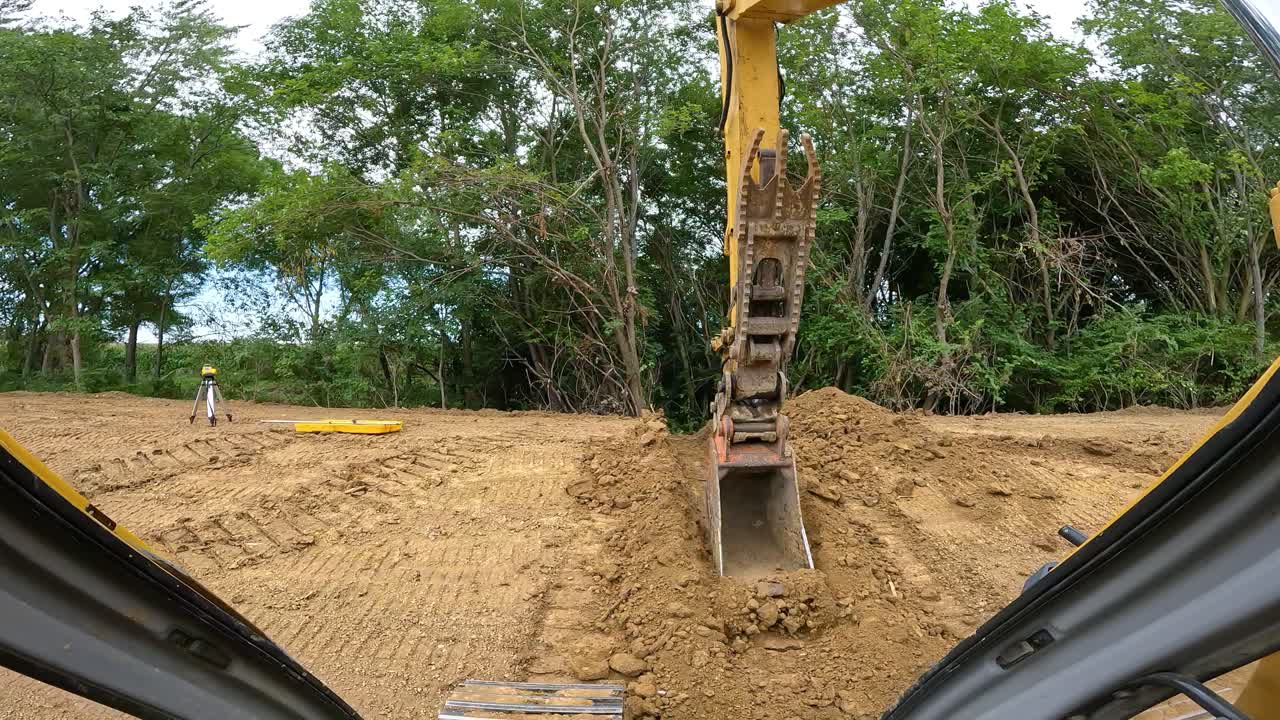 pov mientras opera una gran excavadora hidráulica para nivelar el fondo de la zanja de drenaje de desbordamiento en el sitio de construcción del estanque