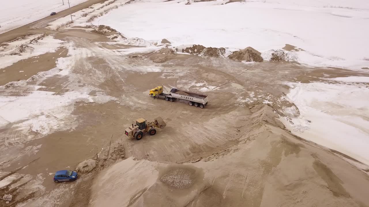 A drone captures a high-angle view of a construction site as a truck is loaded with sand, showcasing industrial machinery in action