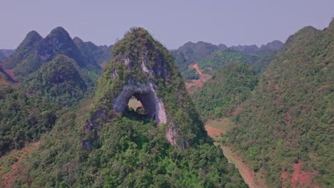 the drone flies over the unique mat than mountain with a large hole in the middle, showcasing the lush green landscape and the remarkable natural formation