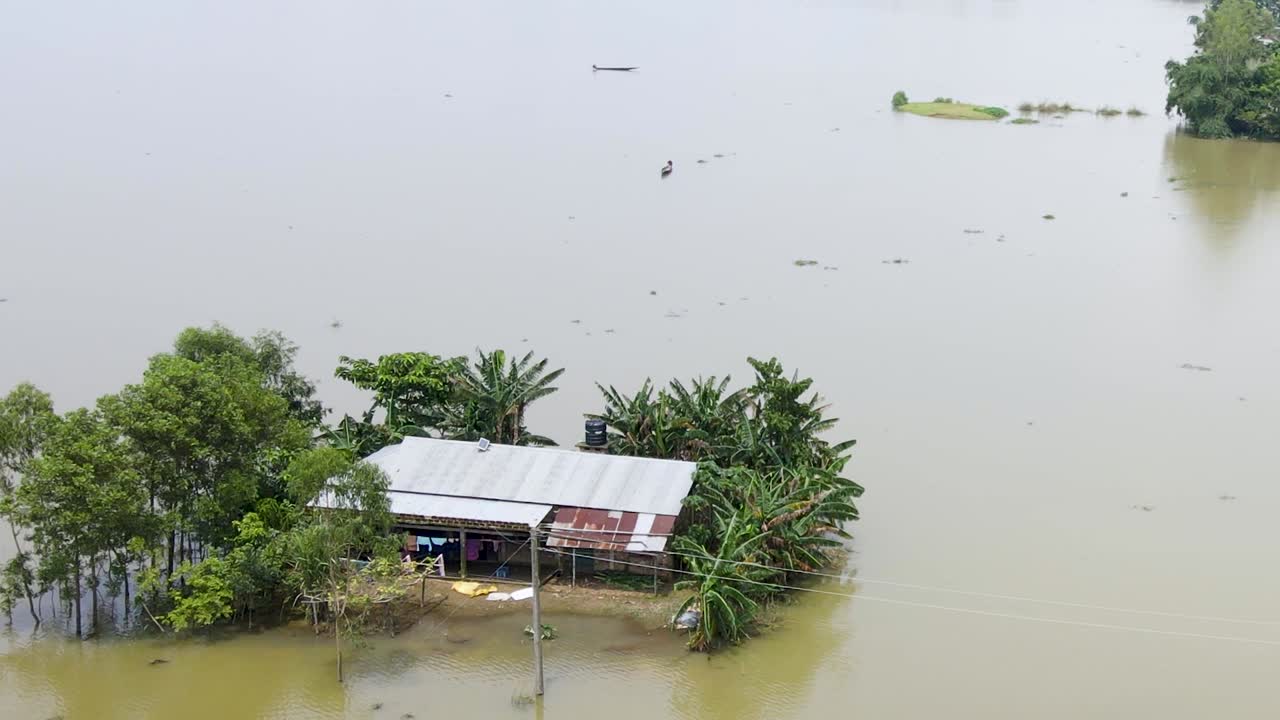 Aerial shot of a rural house with trees isolated by flood water. Bangladesh, South Asia - Sylhet. Boats navigating nearby.