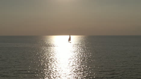 Eine-Schwenkende-Luftaufnahme-Eines-Segelboots-Auf-Einem-See-Bei-Sonnenuntergang