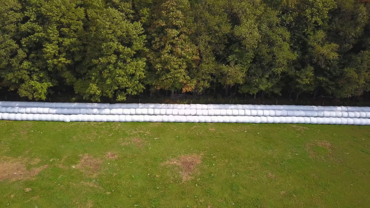 вид с воздуха на ряды тюков сена, выстроившихся в ряд на фермерском поле