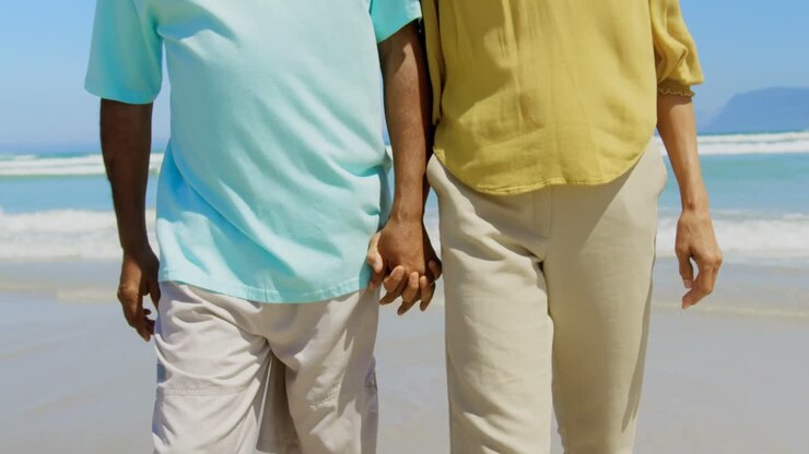 Mid section of active senior African American couple holding hands and walking on the beach 4k