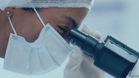 científica con máscara de protección y guantes usando el microscopio