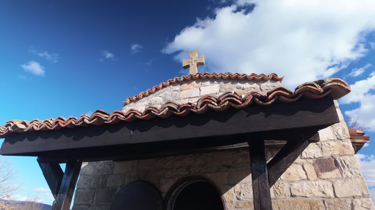 Looking up heavenwards at the entrance of a small chapel, featuring a cross atop its tiled roof.