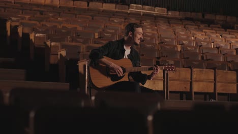 a handsome guy plays an acoustic guitar in an abandoned cinema. the musician sings a song and accompanies on the guitar