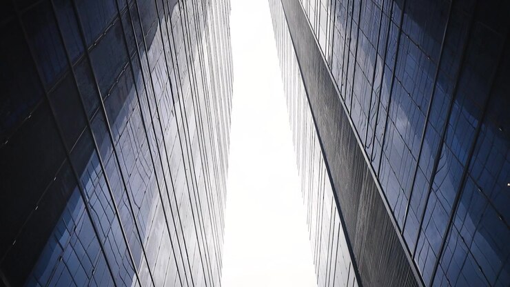 Una vista mirando hacia arriba entre dos modernos edificios de cristal hacia un cielo brillante.