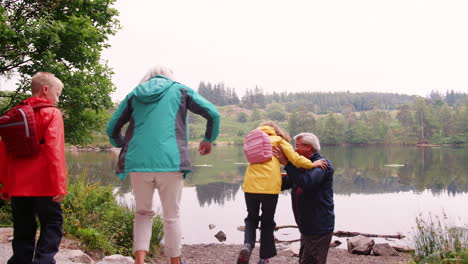 Grandparents-and-grandchildren-have-fun-playing-by-a-lake,-Lake-District,-UK