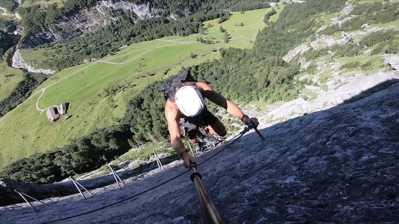A young man exploring the Swiss Alps while climbing up the mountain by carabiner and rope to Furenalp via Ferrata