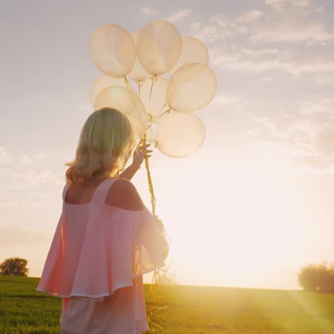 Carefree-Young-Woman-With-Balloons-Walking-On-A-Green-Meadow-At-Sunset-3