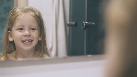 la niña mira los dientes limpios y grita en el espejo grande