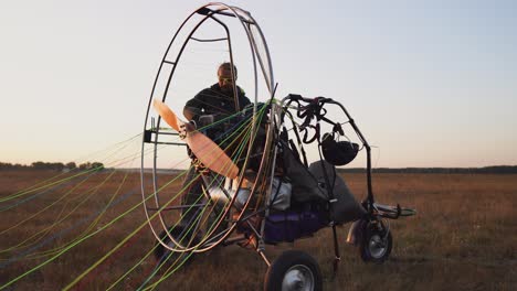 a man pilot of a motor paraglider attaches the parachute to the body of the paraglider preparing for flight and checking equipment