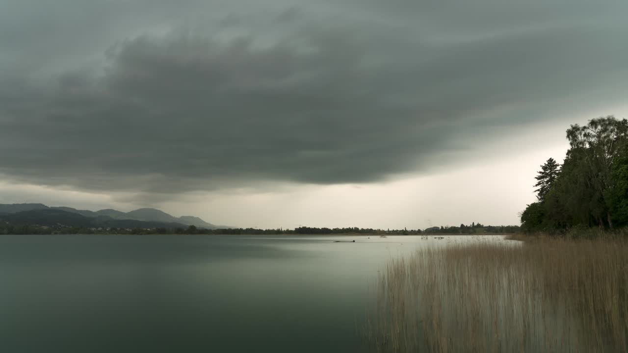 nubes de tormenta grises pasan a través del cielo blanco sobre el borde del lago con una pared de lluvia en wetzikon, suiza, ángulo amplio