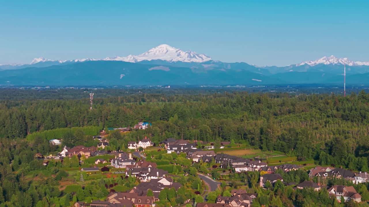 A scenic shot of Langley Township under a clear blue sky surrounded by lush green trees with Mt Baker on the horizon