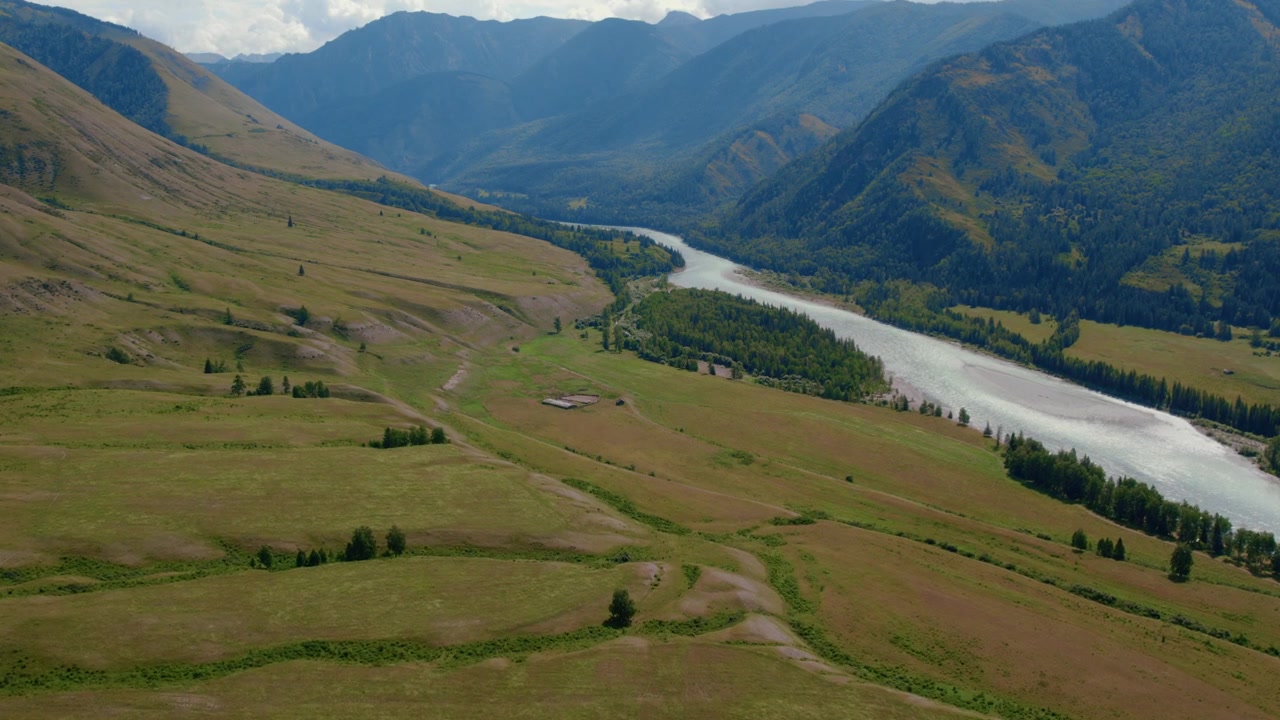 Ampie riprese aeree della Valle di Ak-Kem con un fiume serpeggiante, prati verdi e pendii montuosi boscosi nella Repubblica dell'Altai, Russia, un paesaggio estivo.