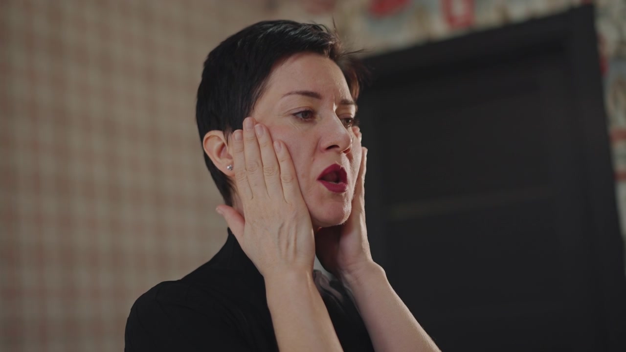 Vocal coach donna che si esercita con il riscaldamento vocale in un'accogliente aula studio, con le mani a coppa sul viso per la risonanza, la bocca aperta che forma le vocali, esercizi di respirazione e controllo dell'intonazione mirati, attenta