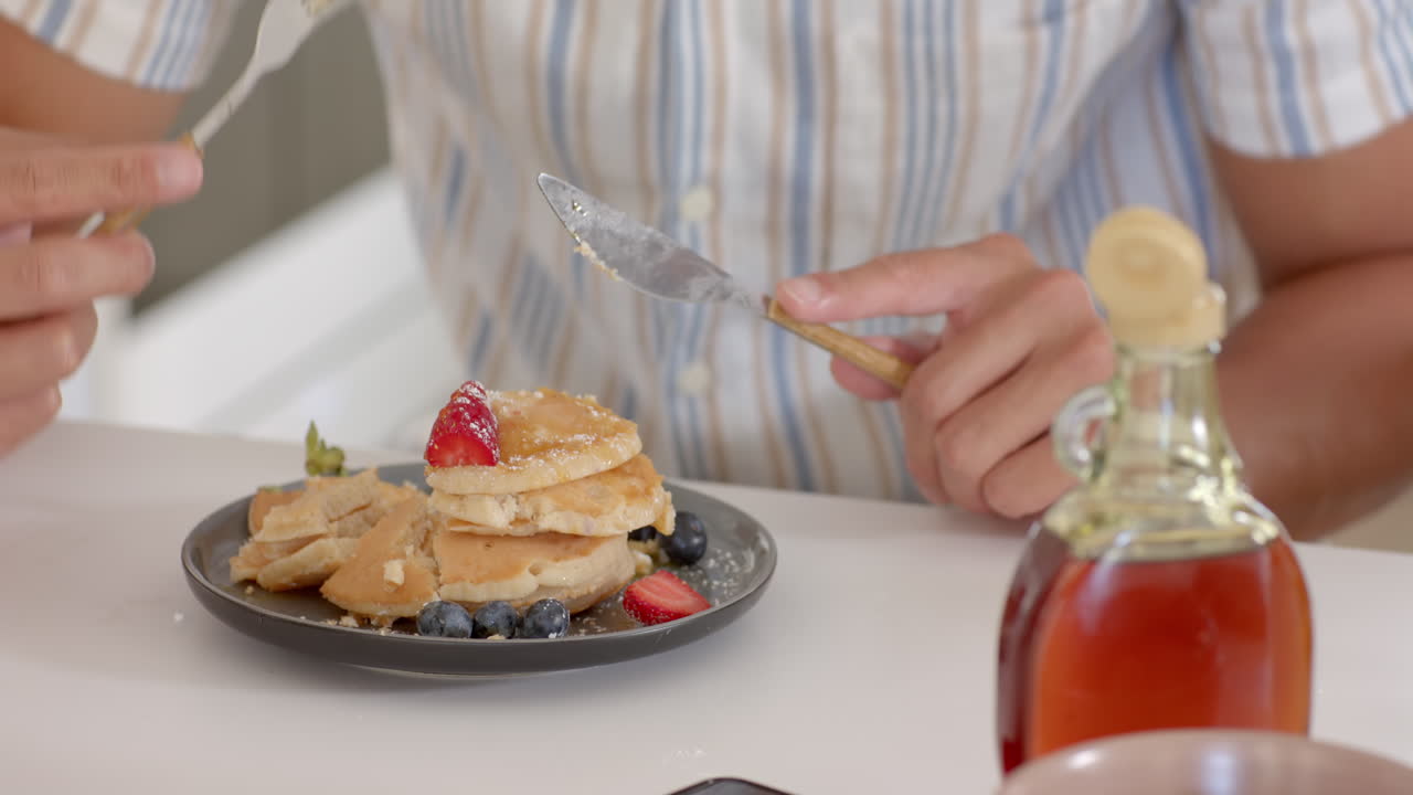 Pouring syrup over pancakes with fresh berries, enjoying breakfast at home