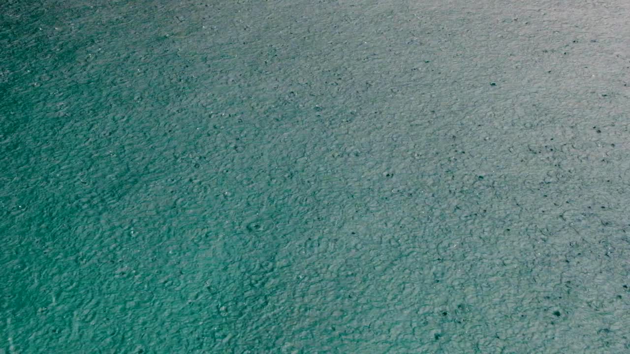 Close up of raindrops during rain downpour onto turquoise ocean water