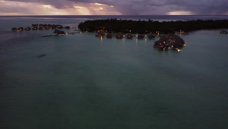 Dusk-aerial-rotates-over-illuminated-tourist-Polynesia-lagoon-cabanas