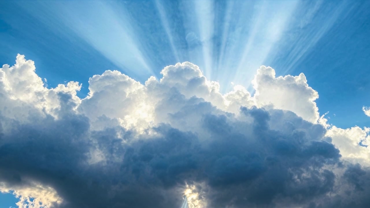 Raggi di Sole che si Irradiano Attraverso Nuvole Bianche e Soffici nel Cielo Blu