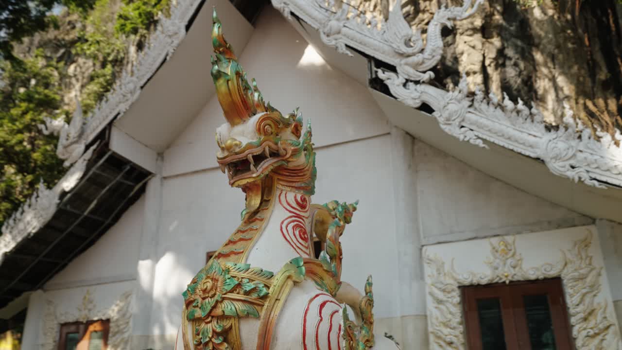 An ornate mythical guardian statue rises beside lush cliffs under bright sunlight in Thailand
