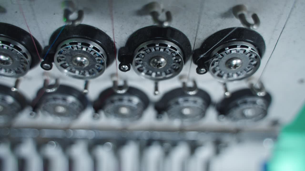 Row of embroidery machine bobbins in multi color machine stitching in synchronized motion threading base layer below