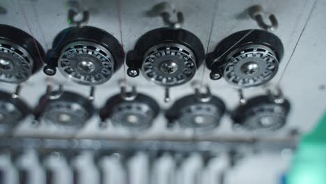 row of embroidery machine bobbins in multi color machine stitching in synchronized motion threading base layer below