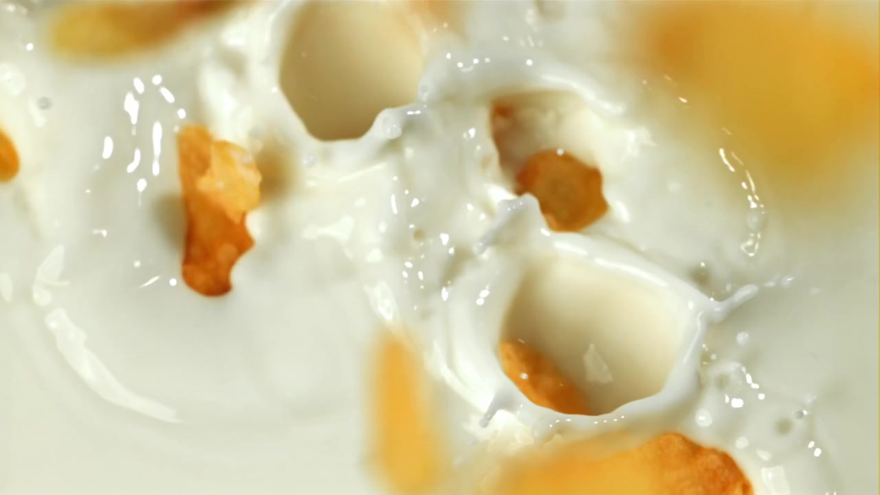 Cornflakes dorati che cadono nel latte bianco fresco al rallentatore