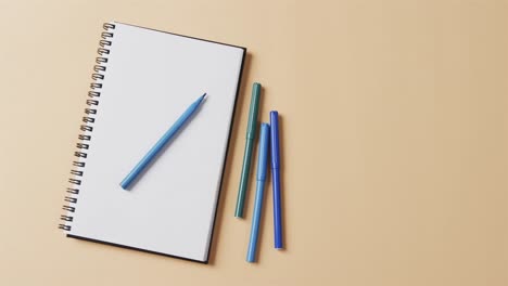 overhead view of blue markers with notebook with copy space on beige background, in slow motion