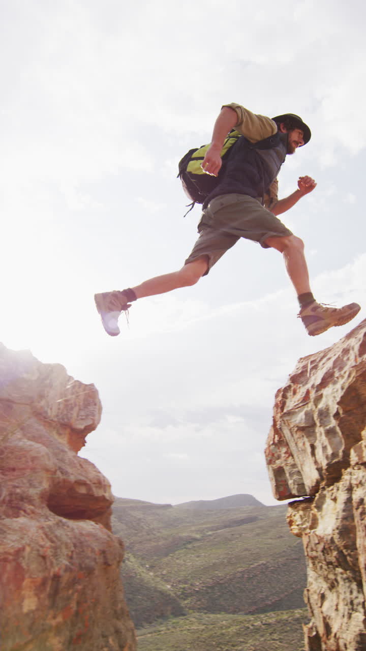 video vertical de un sobreviviente caucásico barbudo explorando el desierto saltando a través de un barranco