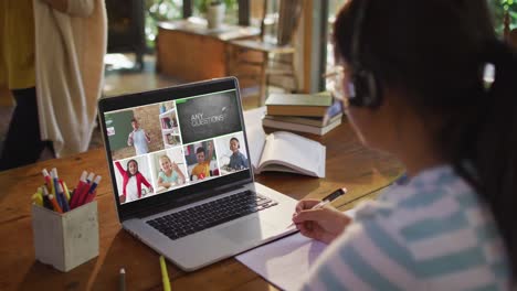 Schoolgirl-using-laptop-for-online-lesson-at-home,-with-diverse-teacher-and-class-on-screen