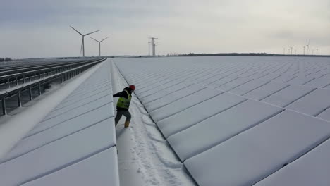 worker inspects snow-covered solar panels at a renewable energy site