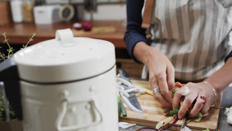 sección media de una mujer biracial compostando residuos de verduras en la cocina, en cámara lenta