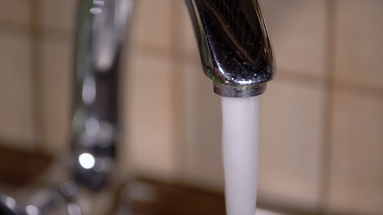 Acqua del rubinetto che scorre da un rubinetto nel lavello di una cucina domestica, primo piano al rallentatore