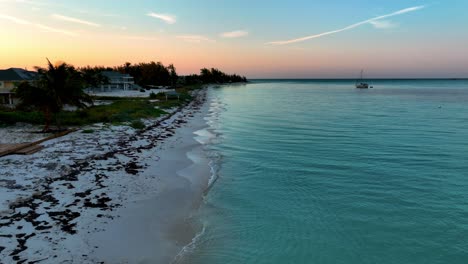 Preciosa-Playa-De-Bahamas-Con-Velero,-Vista-Aérea-Del-Atardecer,-Arenas-Blancas-Y-Aguamarina