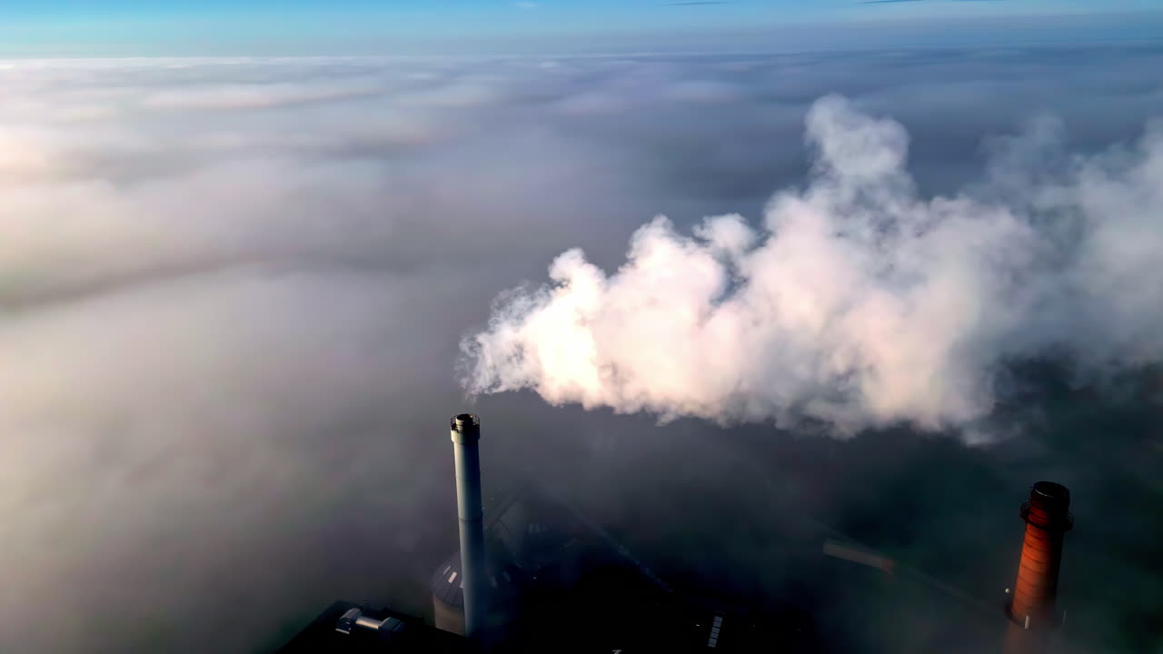 Aerial view orbiting a smoking industrial chimney, in middle of morning fog
