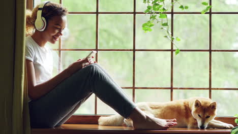teenage girl relaxing at a window with headphones and dog